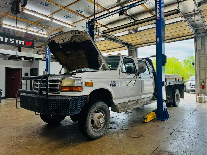 White Ford diesel pickup with the hood open on a lift at Elite Diesel & Auto Works