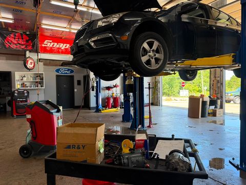 Black Chevrolet Cruze raised on a two-post lift during A/C work, with A/C compressors and parts on a cart in the foreground
