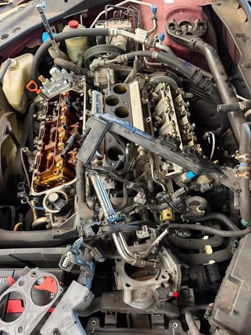 Gas V6 engine in a maroon car with the intake manifold and valve covers removed, showing the camshafts and rocker arms