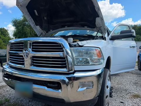 White Ram heavy-duty pickup with the hood up and the driver's door open, parked on gravel