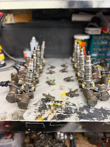 Two rows of diesel fuel injectors set up on a workbench, with hold-down clamps laid out between them