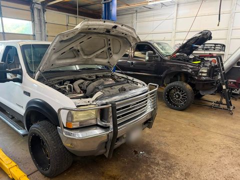 White Ford F-250 Super Duty and a lifted black Ford Super Duty side by side in the shop, both with their hoods open