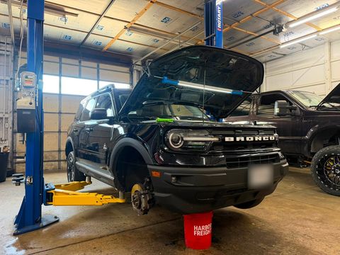 Black Ford Bronco Sport raised on a two-post lift with the front wheel off, exposing the brake rotor
