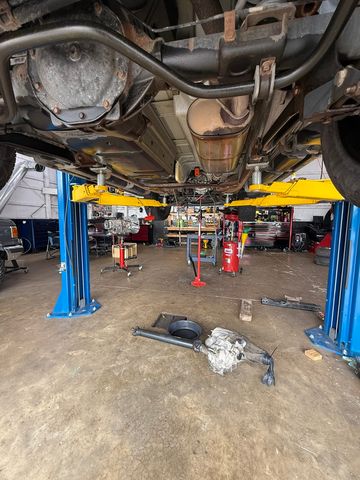 Underside of a vehicle on a lift, with the driveshaft and transfer case removed on the floor below