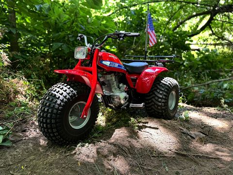 Red vintage Honda three-wheeler parked on a wooded trail