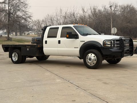 White Ford F-550 crew-cab flatbed truck with a black grille guard