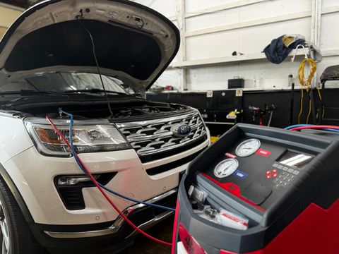White Ford Explorer with the hood up, connected to an A/C service machine
