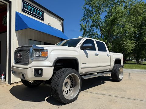 Lifted white GMC Sierra Denali pickup on large wheels outside the shop