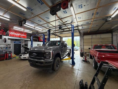 Wide view inside the shop: a gray Ford Super Duty on a two-post lift, a white Chevrolet sedan with its hood up and a red pickup in the next bay