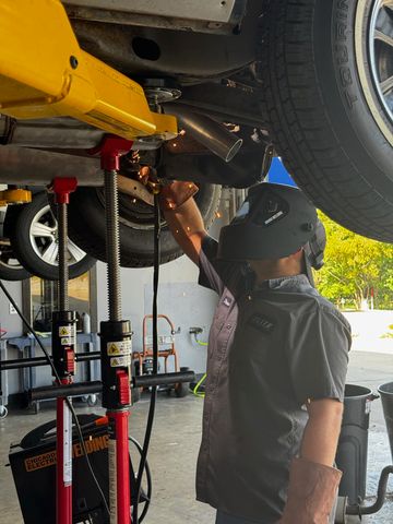 Elite technician in a welding helmet welding an exhaust pipe under a car on a lift
