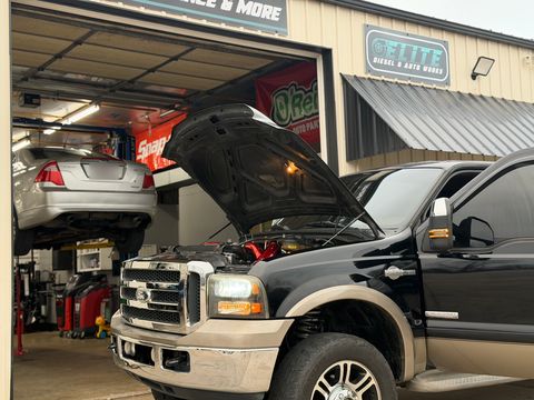 Black Ford F-350 King Ranch with the hood open in front of the shop, a silver sedan on a lift inside