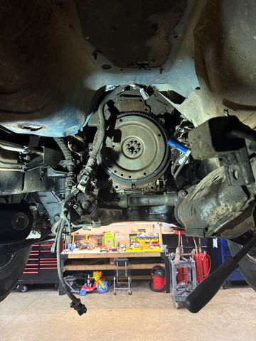 Flywheel exposed with the transmission removed, seen from under a truck on a lift