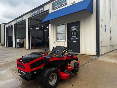 Red zero-turn mower parked outside the shop entrance